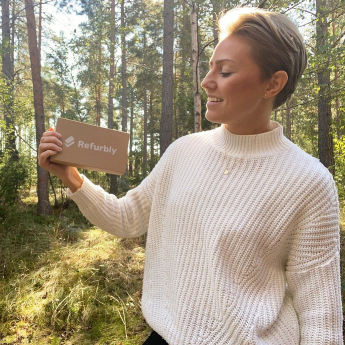 Glad kvinna håller upp Refurbly mobillåda i skog